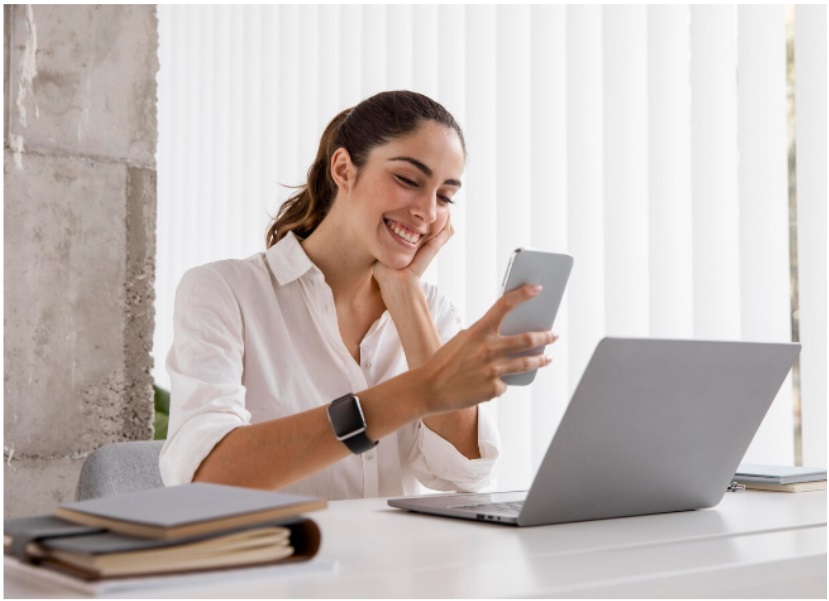 ¿Por qué mis correos electrónicos son marcados como spam? 1 Mujer sonriente revisando correos electrónicos marcados como spam en su teléfono y laptop en una oficina.