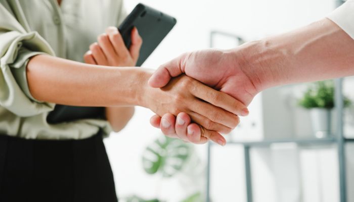 Blog 7 Apretón de manos entre dos profesionales, uno sosteniendo un teléfono inteligente, simbolizando el inicio de relaciones comerciales duraderas